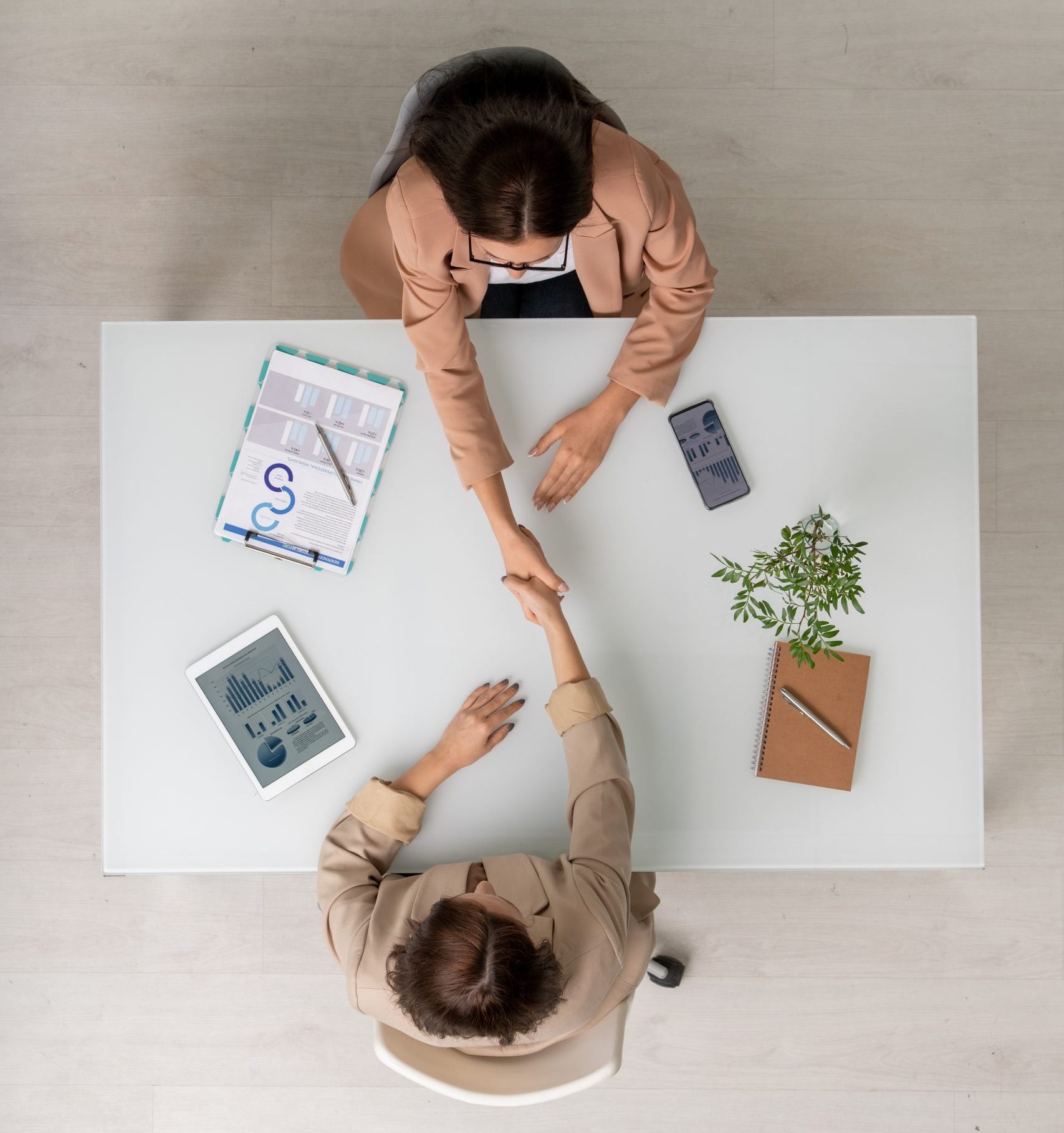 Top view of two elegant businesswomen shaking hands over desk after negotiating