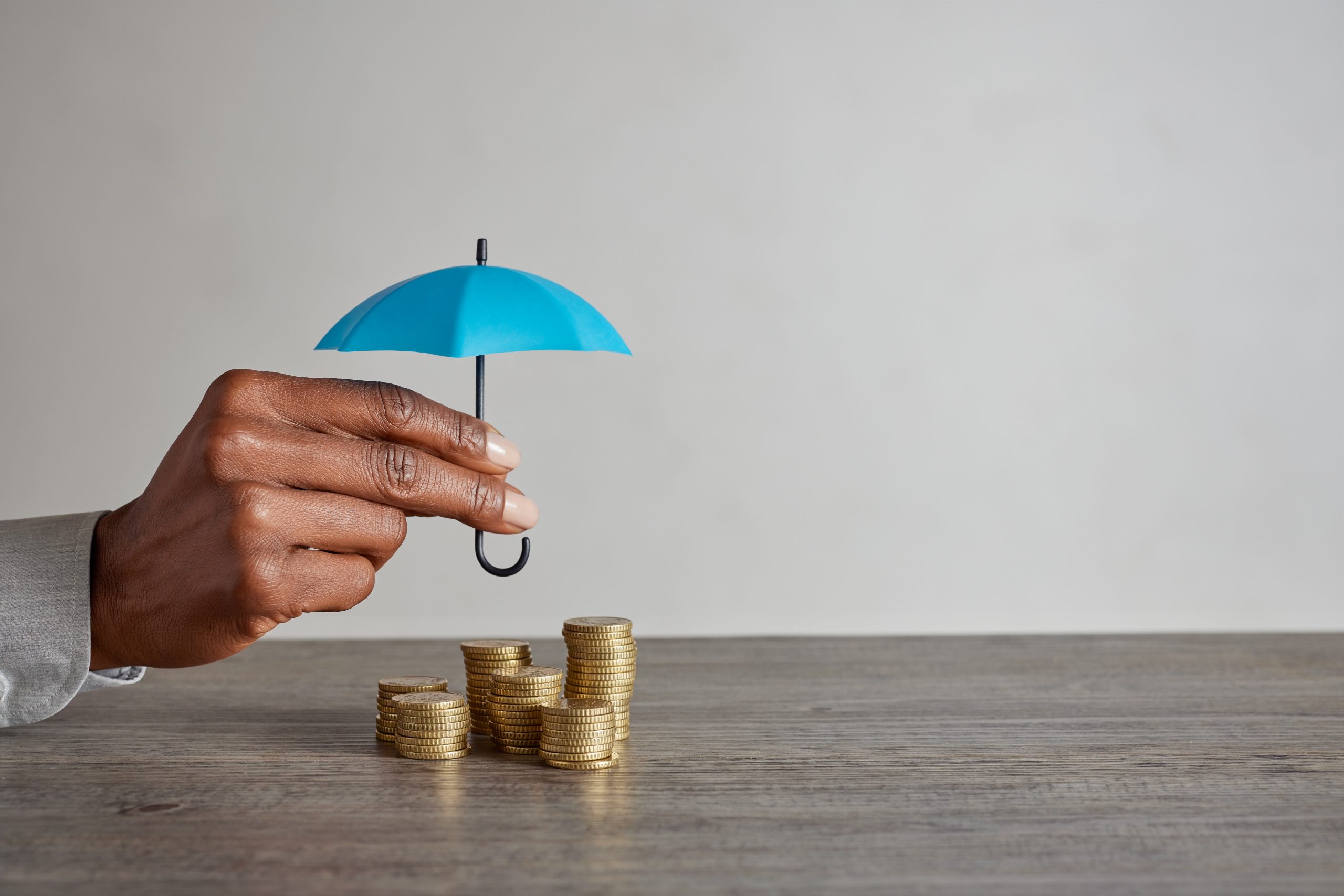 Black woman hand holding umbrella over money to protect her savi protecting money