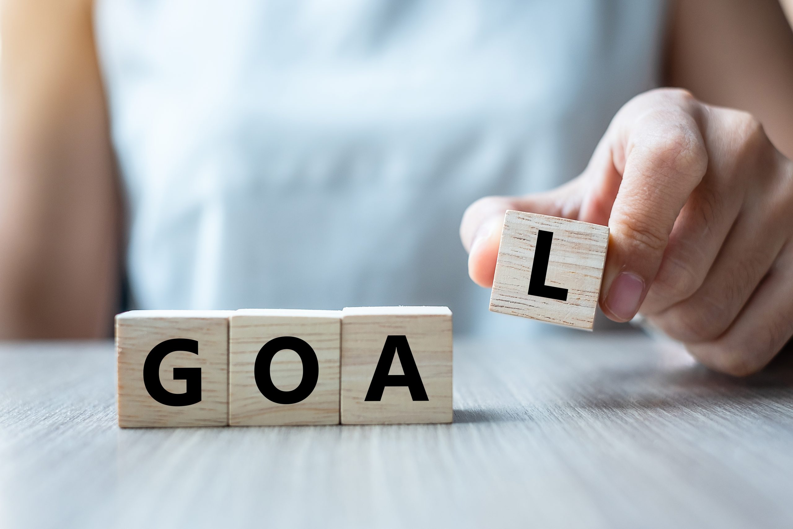 Businesswoman hand holding wooden cube with GOAL text on table b goal